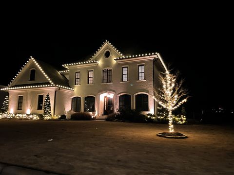 Warm white C9 roofline lights and a wrapped tree on a brick two-story home in Cary, NC