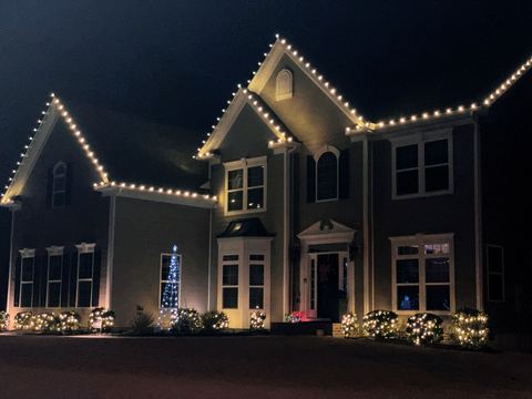 Warm white C9 roofline lights and lit bushes on a two-story colonial home in Cary, NC
