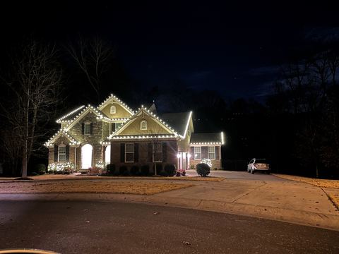 Warm white C9 lights along every peak on a stone and brick two-story home in Cary, NC