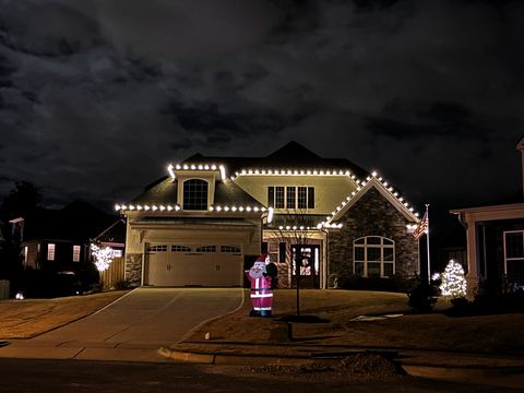 Warm white C9 roofline lights and a lit dormer on a stone-front home in Cary, NC