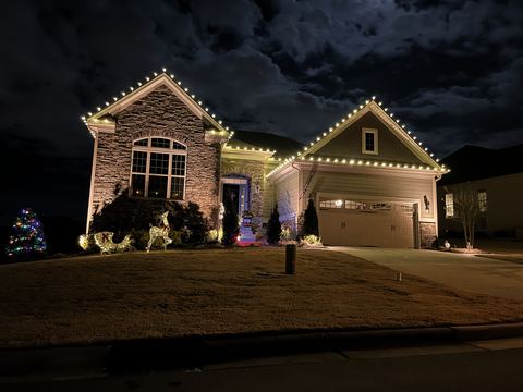 Warm white C9 lights on two front gables on a stone and siding ranch home in Cary, NC